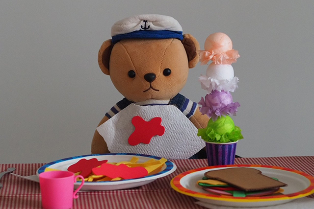 A Teddy bear sitting at a table with toy food