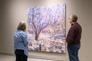 Two people looking at a painting of a forest winter scene